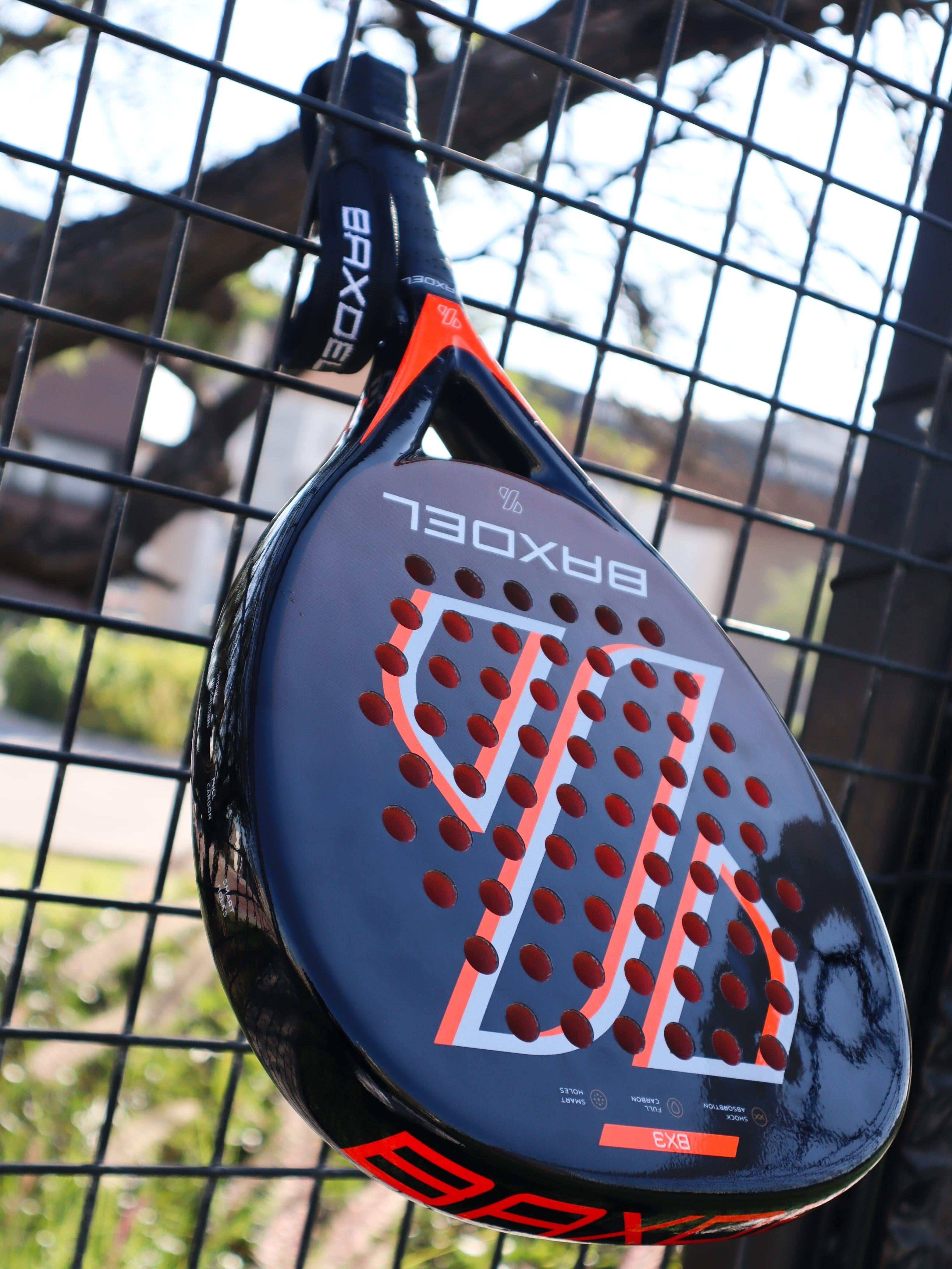 Pala de pádel Baxdel BX-3 apoyada en la reja de una cancha, fabricada en México